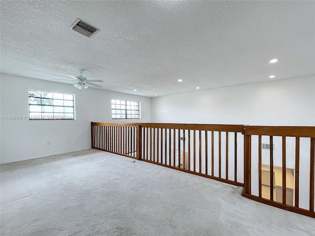 empty room with ceiling fan, a textured ceiling, and light colored carpet