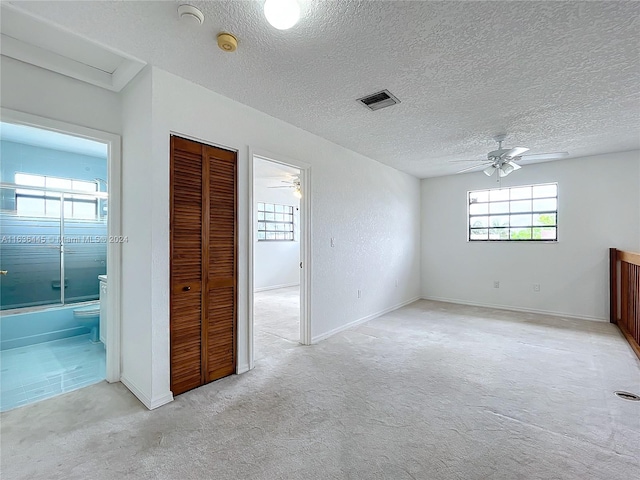 interior space featuring ensuite bath, a textured ceiling, and light colored carpet