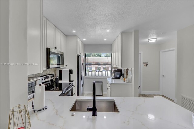 kitchen featuring a textured ceiling, white cabinets, light stone countertops, stainless steel appliances, and sink