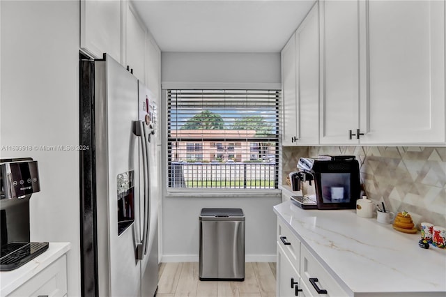 kitchen featuring decorative backsplash, light stone countertops, white cabinetry, light hardwood / wood-style flooring, and stainless steel fridge