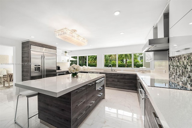 kitchen with a center island, wall chimney exhaust hood, sink, stainless steel built in refrigerator, and a breakfast bar