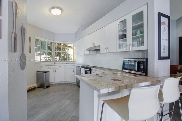 kitchen with appliances with stainless steel finishes, tile countertops, backsplash, white cabinetry, and kitchen peninsula