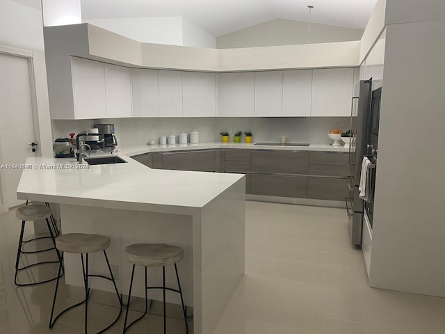 kitchen featuring lofted ceiling, light tile patterned floors, a kitchen breakfast bar, sink, and kitchen peninsula