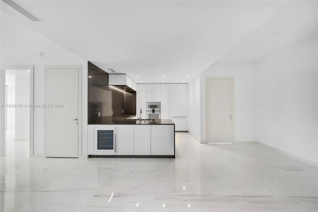 kitchen with stainless steel microwave, sink, beverage cooler, and white cabinetry