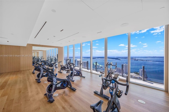 exercise room with a wall of windows, a water view, and light hardwood / wood-style floors