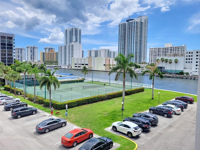 view of vehicle parking with tennis court, a water view, and a yard