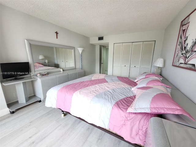 bedroom with a textured ceiling, light wood-type flooring, and a closet