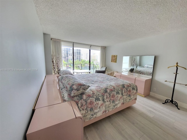 bedroom featuring a wall of windows, access to outside, a textured ceiling, and light hardwood / wood-style floors