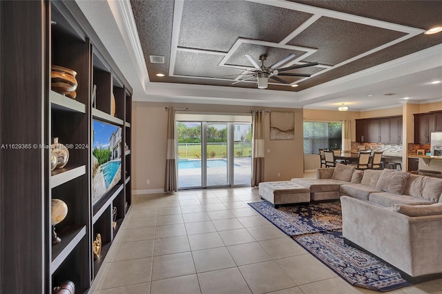 living room with a textured ceiling, a tray ceiling, light tile patterned floors, and ceiling fan