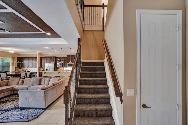 staircase with tile patterned floors and a raised ceiling