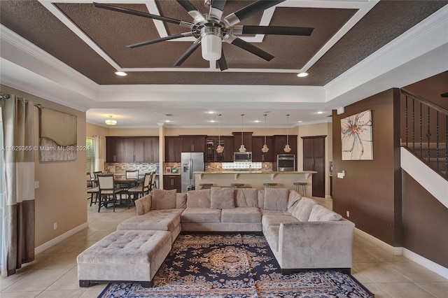 tiled living room with a raised ceiling, crown molding, and ceiling fan