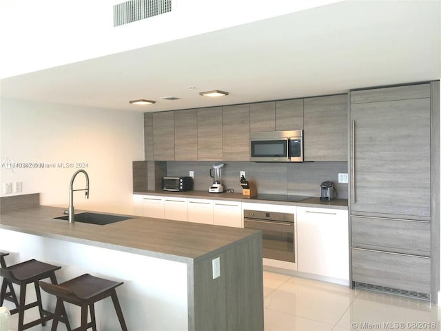 kitchen with decorative backsplash, appliances with stainless steel finishes, a breakfast bar area, sink, and kitchen peninsula