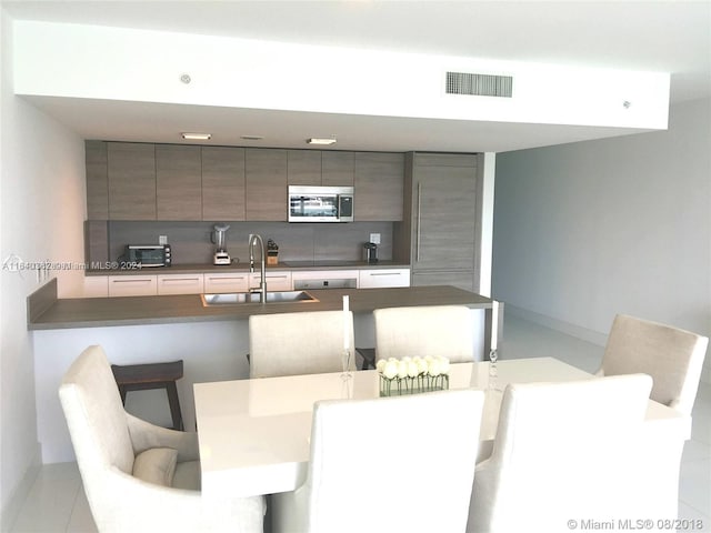 400 Sunny Isles Blvd Unit 1019, Sunny Isles Beach, FL 33160 - kitchen with stainless steel microwave, modern cabinets, a breakfast bar, backsplash, and dark countertops