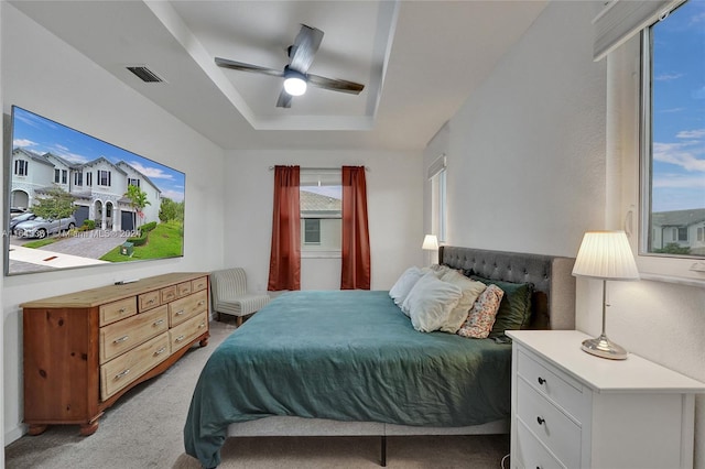 bedroom with light carpet, ceiling fan, and a raised ceiling