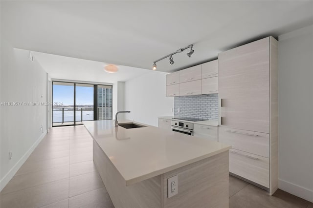 kitchen with decorative backsplash, sink, floor to ceiling windows, a center island with sink, and track lighting