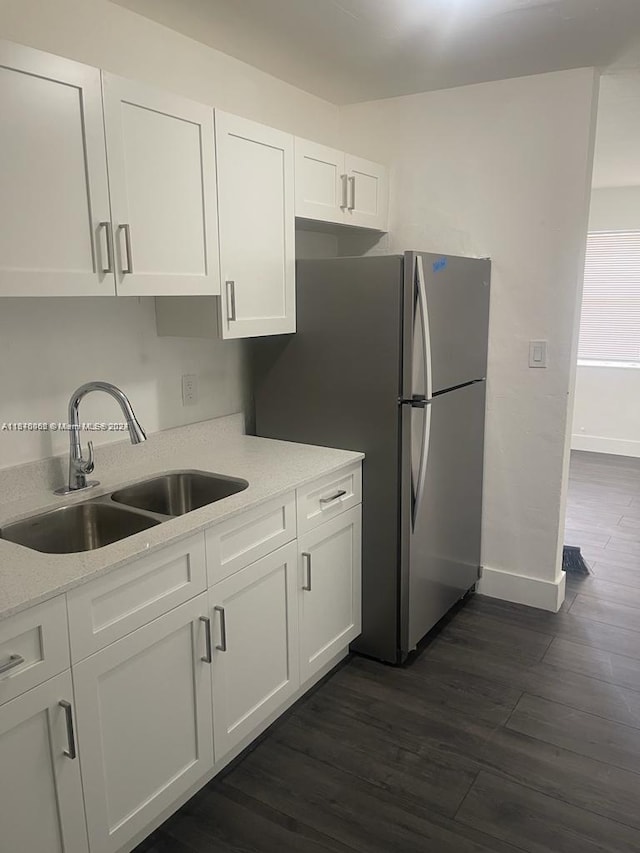 kitchen with a sink, white cabinetry, baseboards, freestanding refrigerator, and dark wood finished floors
