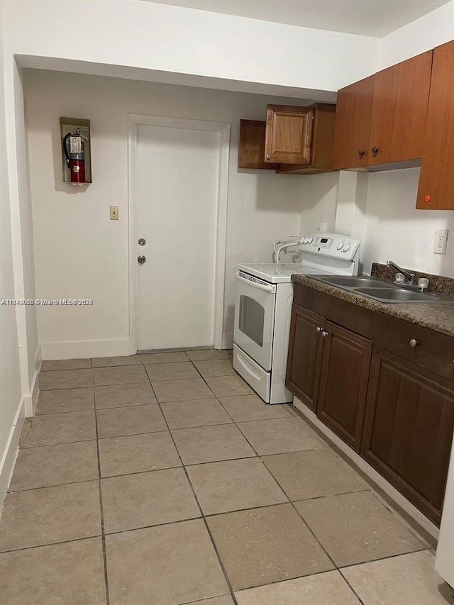 kitchen featuring light tile patterned floors, a sink, white range with electric stovetop, dark countertops, and baseboards