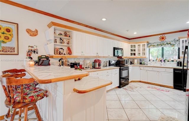 kitchen featuring a breakfast bar area, black appliances, tile counters, kitchen peninsula, and white cabinets