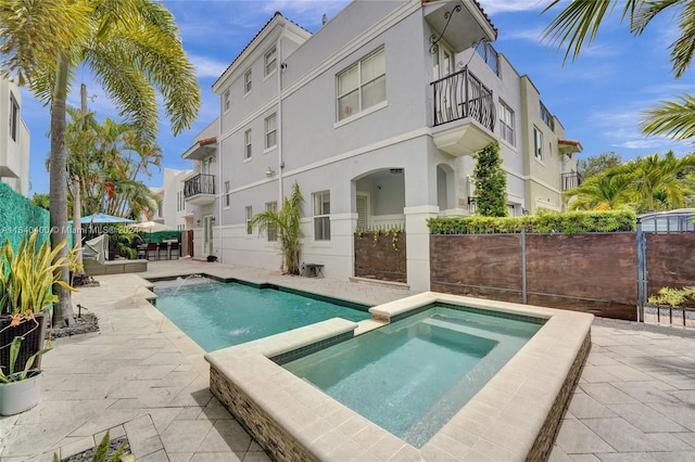 back of property featuring a pool with connected hot tub, fence, and stucco siding