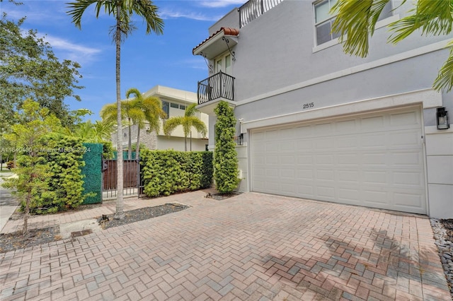 exterior space featuring a garage, a balcony, fence, decorative driveway, and stucco siding