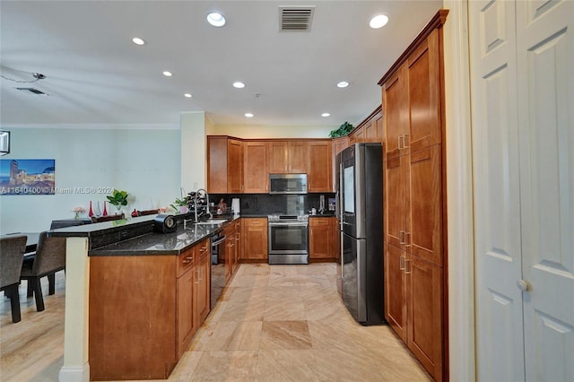 kitchen with a peninsula, a sink, appliances with stainless steel finishes, brown cabinets, and dark stone countertops