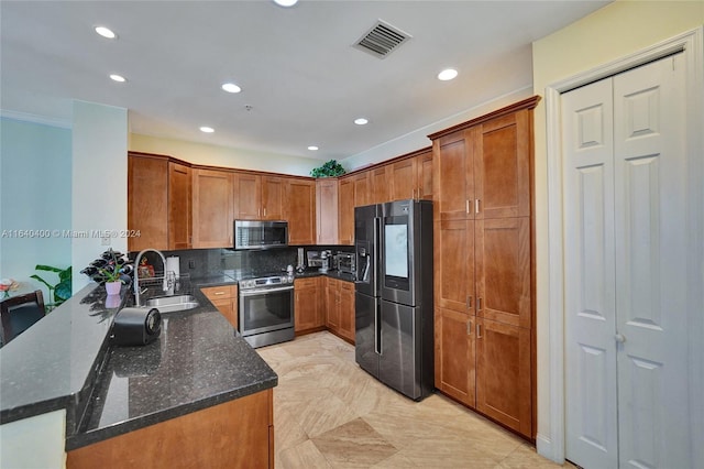 kitchen with brown cabinets, stainless steel appliances, visible vents, a sink, and dark stone countertops