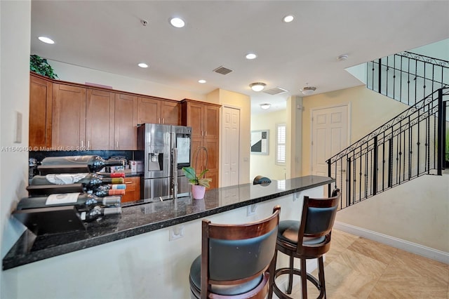 kitchen featuring brown cabinetry, dark stone countertops, stainless steel fridge, and recessed lighting