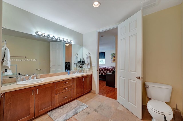 ensuite bathroom featuring a sink, double vanity, toilet, and connected bathroom