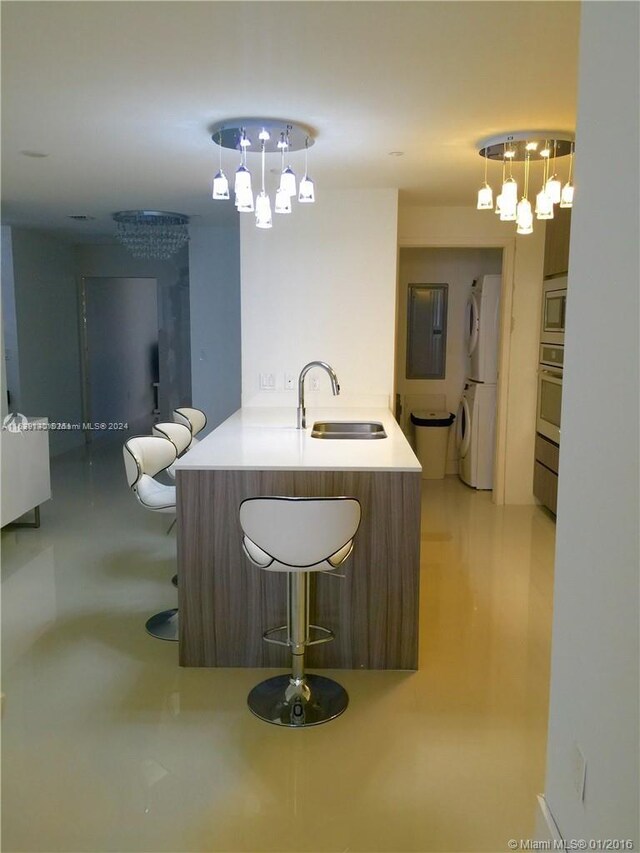 kitchen featuring appliances with stainless steel finishes, stacked washer and clothes dryer, a notable chandelier, decorative light fixtures, and sink