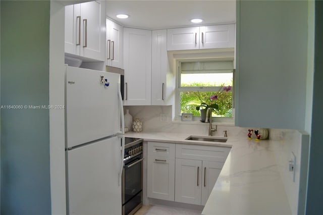 kitchen featuring white refrigerator, light stone countertops, white cabinets, sink, and stove