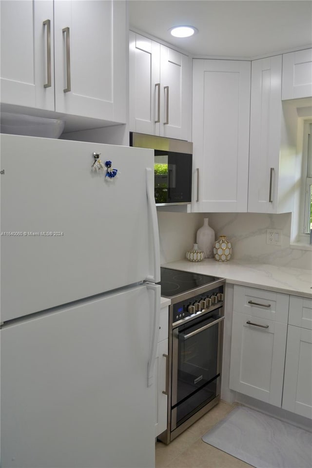 kitchen featuring light tile patterned flooring, light stone countertops, gas range, white cabinets, and white fridge