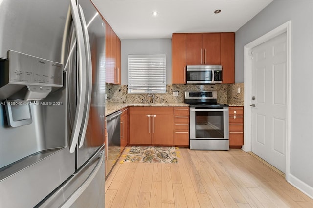 kitchen featuring sink, stainless steel appliances, light stone counters, light hardwood / wood-style floors, and decorative backsplash