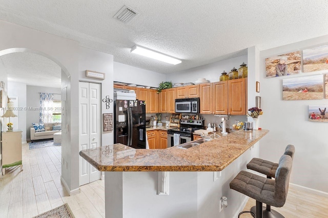 kitchen featuring light wood-type flooring, appliances with stainless steel finishes, kitchen peninsula, and a breakfast bar