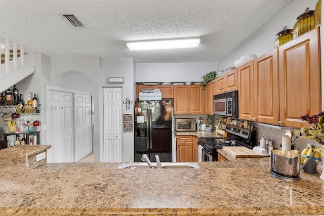 kitchen featuring appliances with stainless steel finishes, light stone countertops, sink, kitchen peninsula, and a textured ceiling