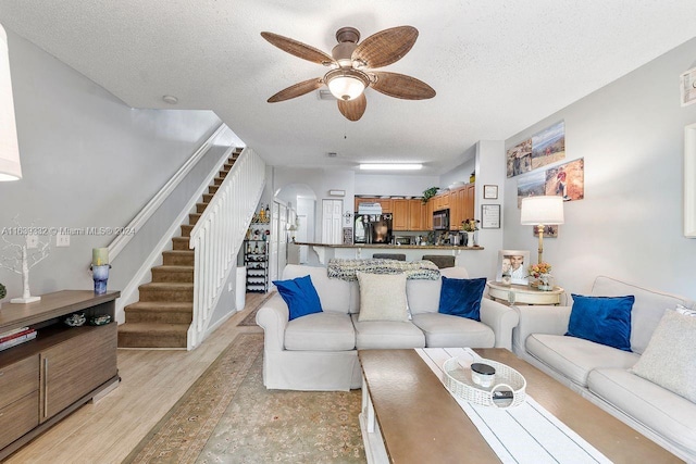 living room featuring a textured ceiling, ceiling fan, and light wood-type flooring