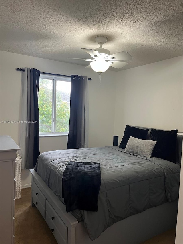 bedroom with a textured ceiling, dark carpet, and ceiling fan