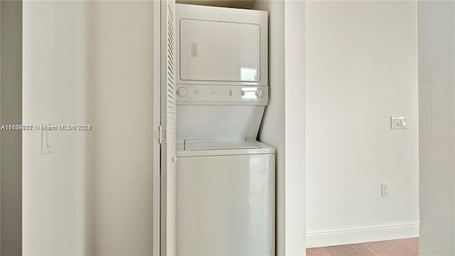 laundry area with hardwood / wood-style flooring and stacked washer and clothes dryer