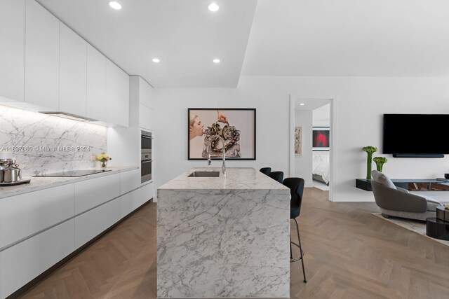 kitchen with a kitchen breakfast bar, white cabinetry, light stone counters, parquet floors, and sink