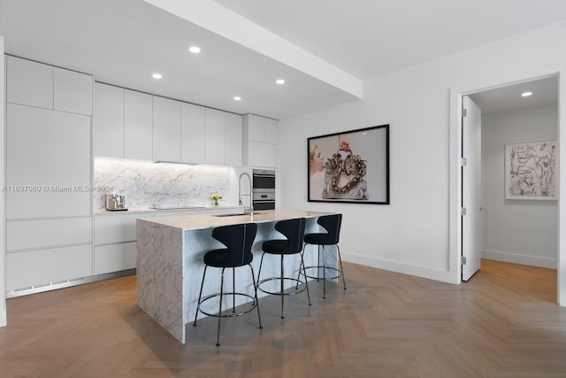 kitchen with a kitchen island with sink, parquet floors, tasteful backsplash, and white cabinets