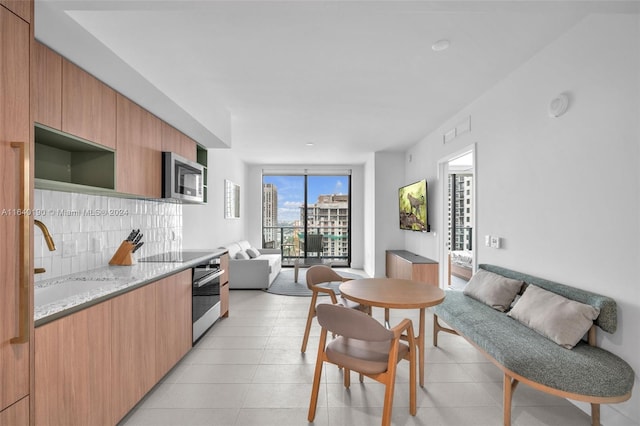 kitchen featuring tasteful backsplash, light tile patterned flooring, stainless steel appliances, light stone countertops, and sink