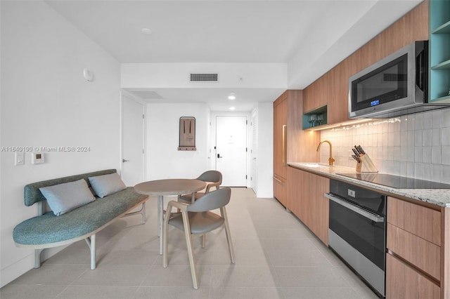 kitchen with decorative backsplash, light stone counters, appliances with stainless steel finishes, light tile patterned floors, and sink