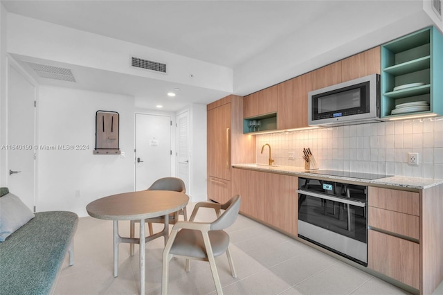 kitchen with black appliances, light stone countertops, light tile patterned flooring, and backsplash