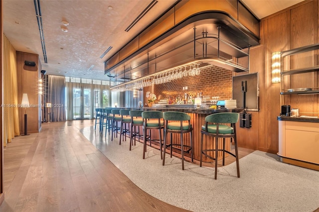 bar with light wood-type flooring, a textured ceiling, and decorative backsplash