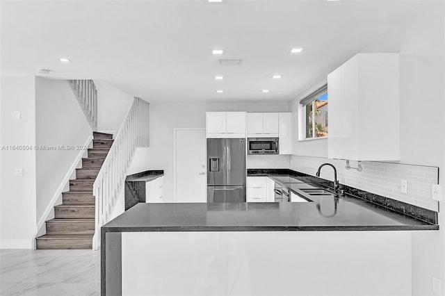 kitchen with tasteful backsplash, sink, white cabinets, kitchen peninsula, and appliances with stainless steel finishes