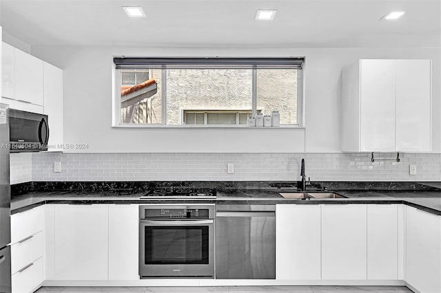 kitchen with dark stone counters, stainless steel appliances, white cabinetry, and sink