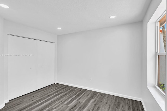 unfurnished bedroom featuring a textured ceiling, a closet, and dark wood-type flooring