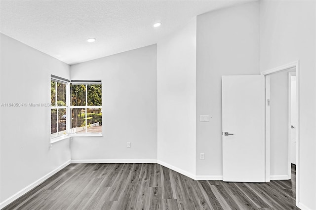 spare room with wood-type flooring, vaulted ceiling, and a textured ceiling