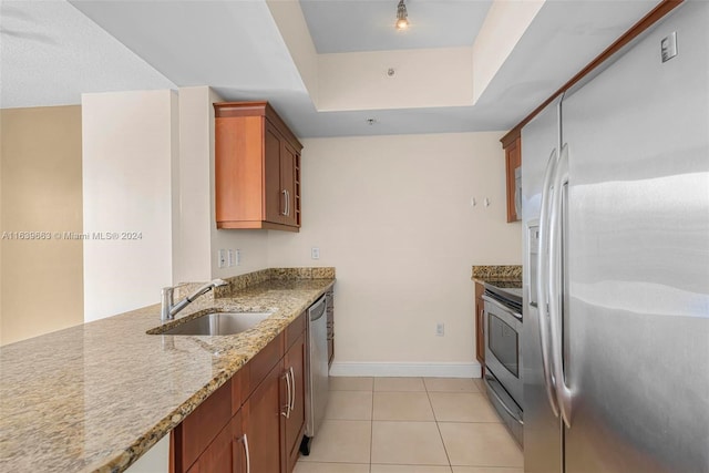 kitchen with appliances with stainless steel finishes, light stone countertops, light tile patterned floors, a tray ceiling, and sink