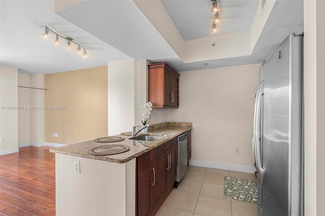 kitchen with appliances with stainless steel finishes, sink, track lighting, and light stone countertops