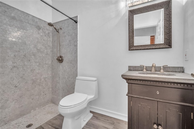 bathroom with wood-type flooring, vanity, tiled shower, and toilet